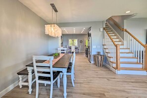 A dining area with a long wooden table and white chairs, a chandelier, and a staircase leading to another level. - Charming Saratoga Lake Retreat w/ Dock Access (Saratoga Springs)