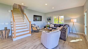 A spacious living room with a wooden staircase, a sofa set, a coffee table, and a floor lamp. - Charming Saratoga Lake Retreat w/ Dock Access (Saratoga Springs)