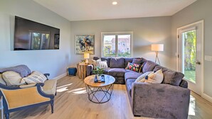 A living room with a sofa, armchair, and coffee table. There are windows, a lamp, and artwork on the walls. - Charming Saratoga Lake Retreat w/ Dock Access (Saratoga Springs)