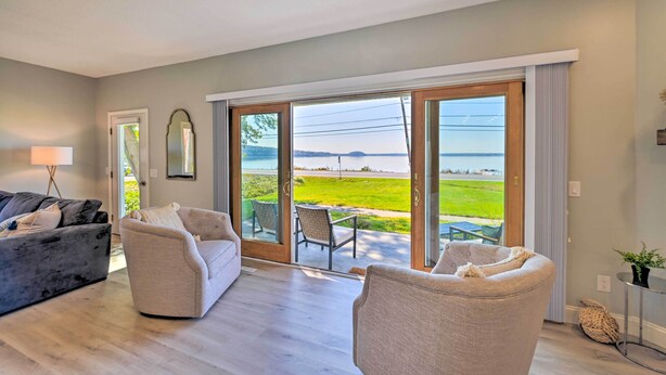 A spacious living room with a large sliding glass door leading to a balcony with a view of a green field and water. - Charming Saratoga Lake Retreat w/ Dock Access (Saratoga Springs)