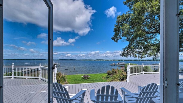Eine Holzterrasse mit Adirondack-Stühlen mit Blick auf einen See, auf dem sich Stege und Boote befinden.
