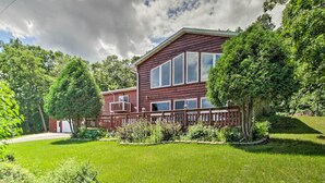 Een houten huis met twee verdiepingen, een omheind erf en een grote boom ervoor.