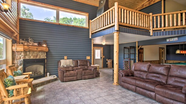 Een ruime woonkamer met een open haard, leren banken, houten meubels en een balkon met houten balustrade.