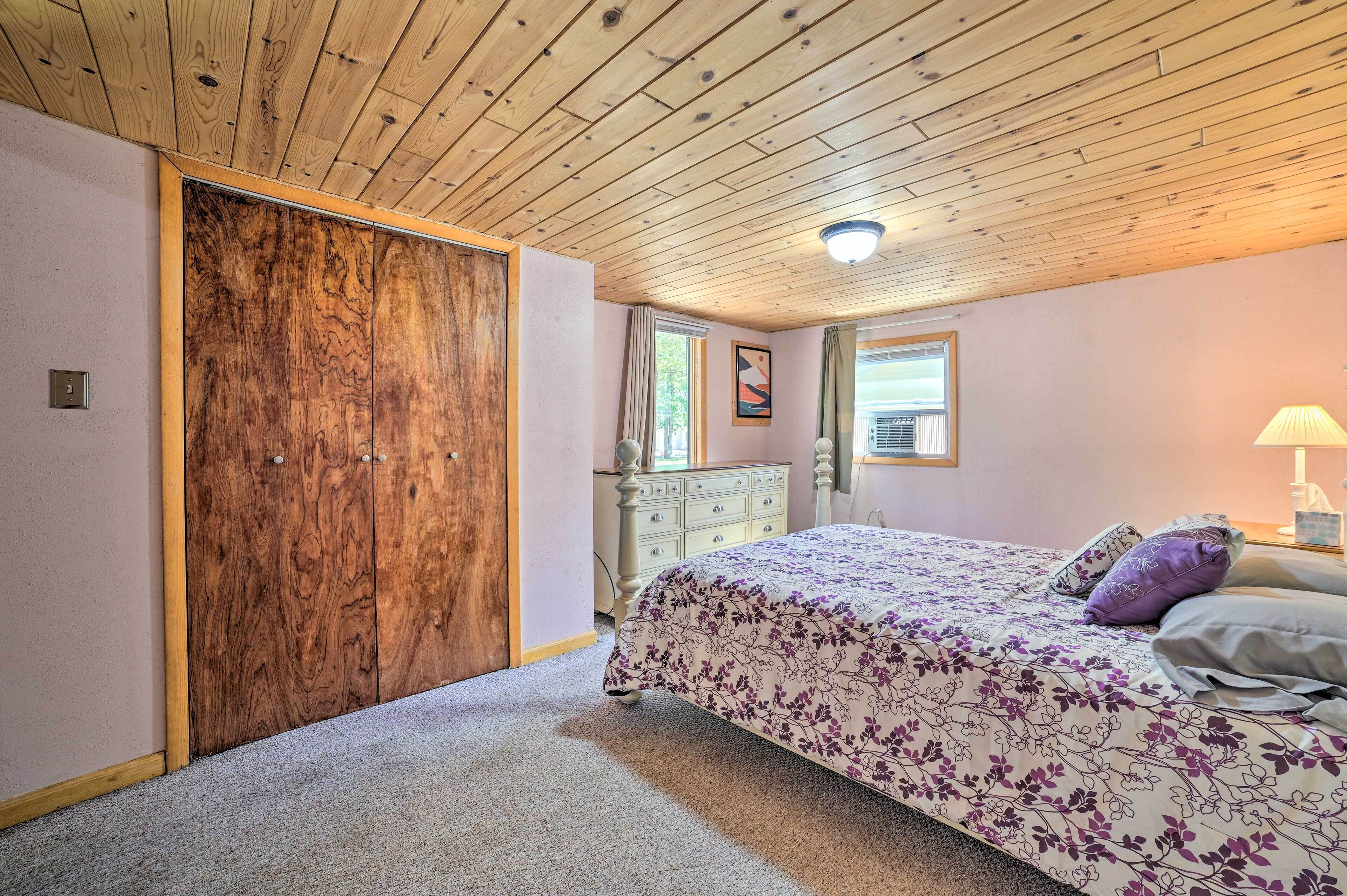 Een slaapkamer met een houten plafond, een bed met bloemenbeddengoed, een dressoir en een raam met gordijnen.