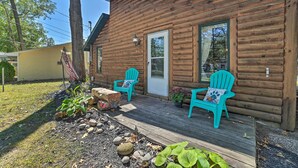 A wooden cabin with a porch, two turquoise Adirondack chairs, and a small garden area with rocks and plants. - Charming Houghton Lake Cottage w/ Backyard! (Prudenville)