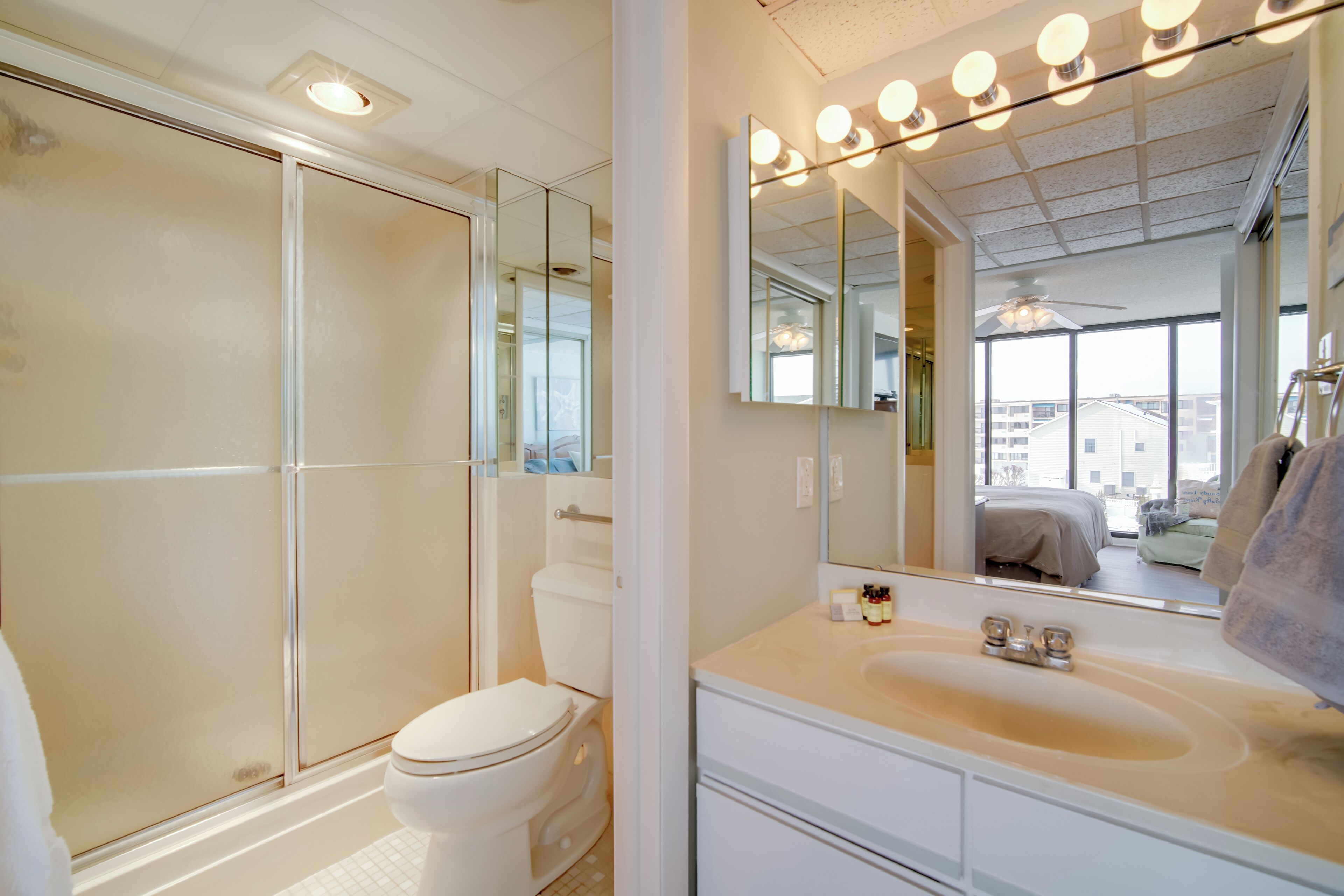 Un baño moderno con cabina de ducha de vidrio, inodoro blanco, tocador con lavamanos y un espejo grande con iluminación.