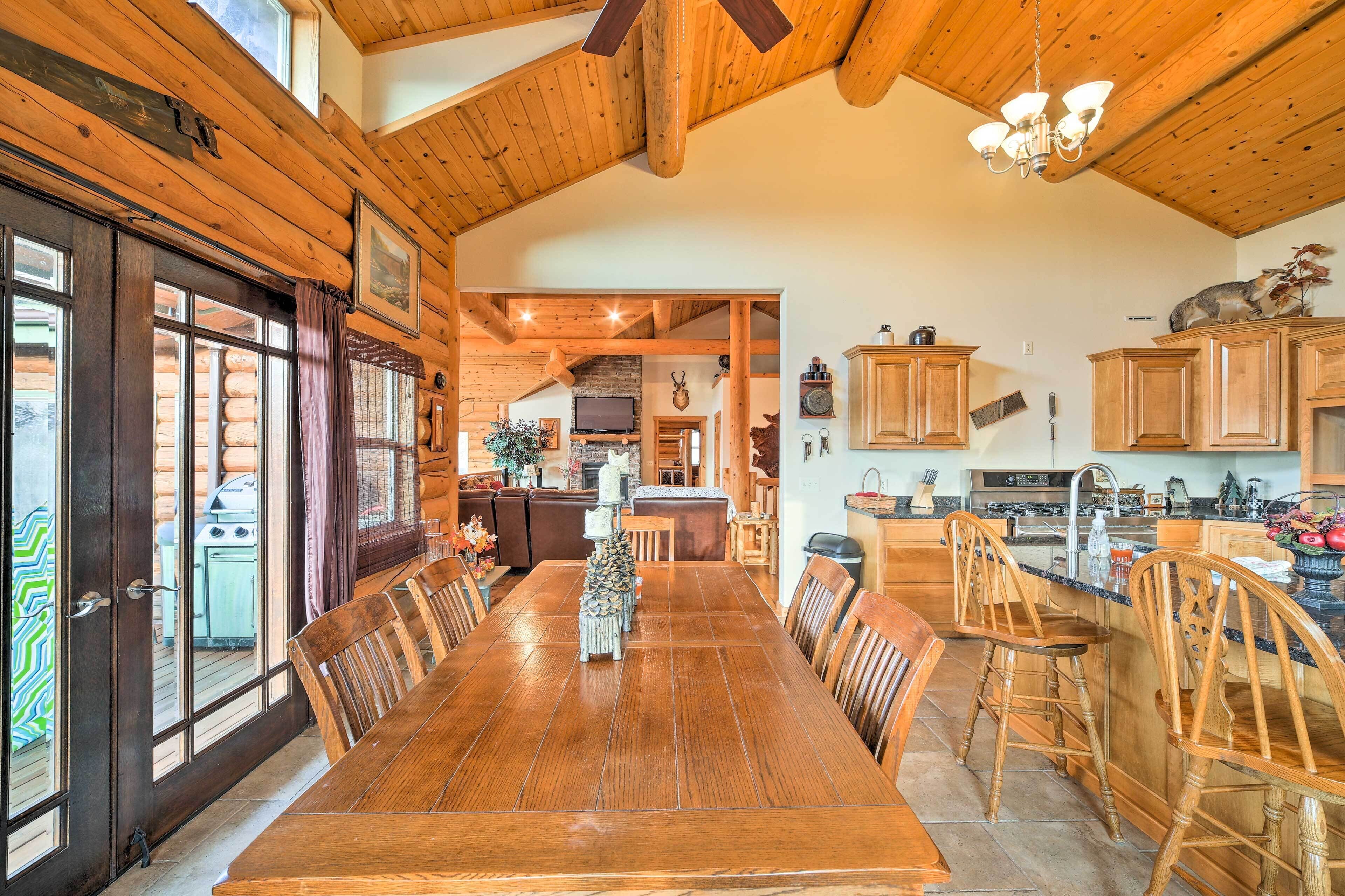 A spacious dining area with a large wooden table and chairs, a kitchen with wooden cabinets, and a high ceiling with exposed beams.