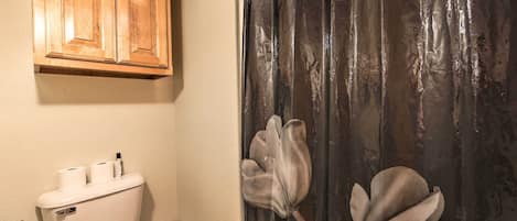 A bathroom with a toilet, wooden cabinets, and a shower curtain with a floral design.