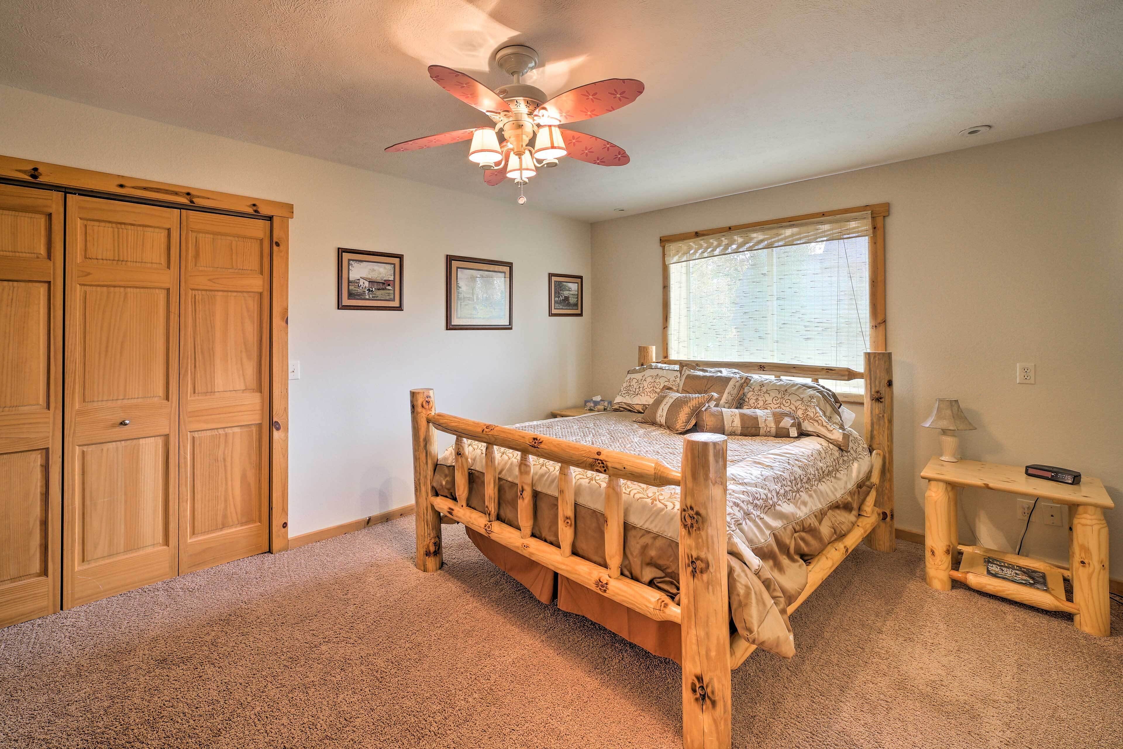 A bedroom with a wooden bed, a ceiling fan, a window with blinds, and a wooden wardrobe.