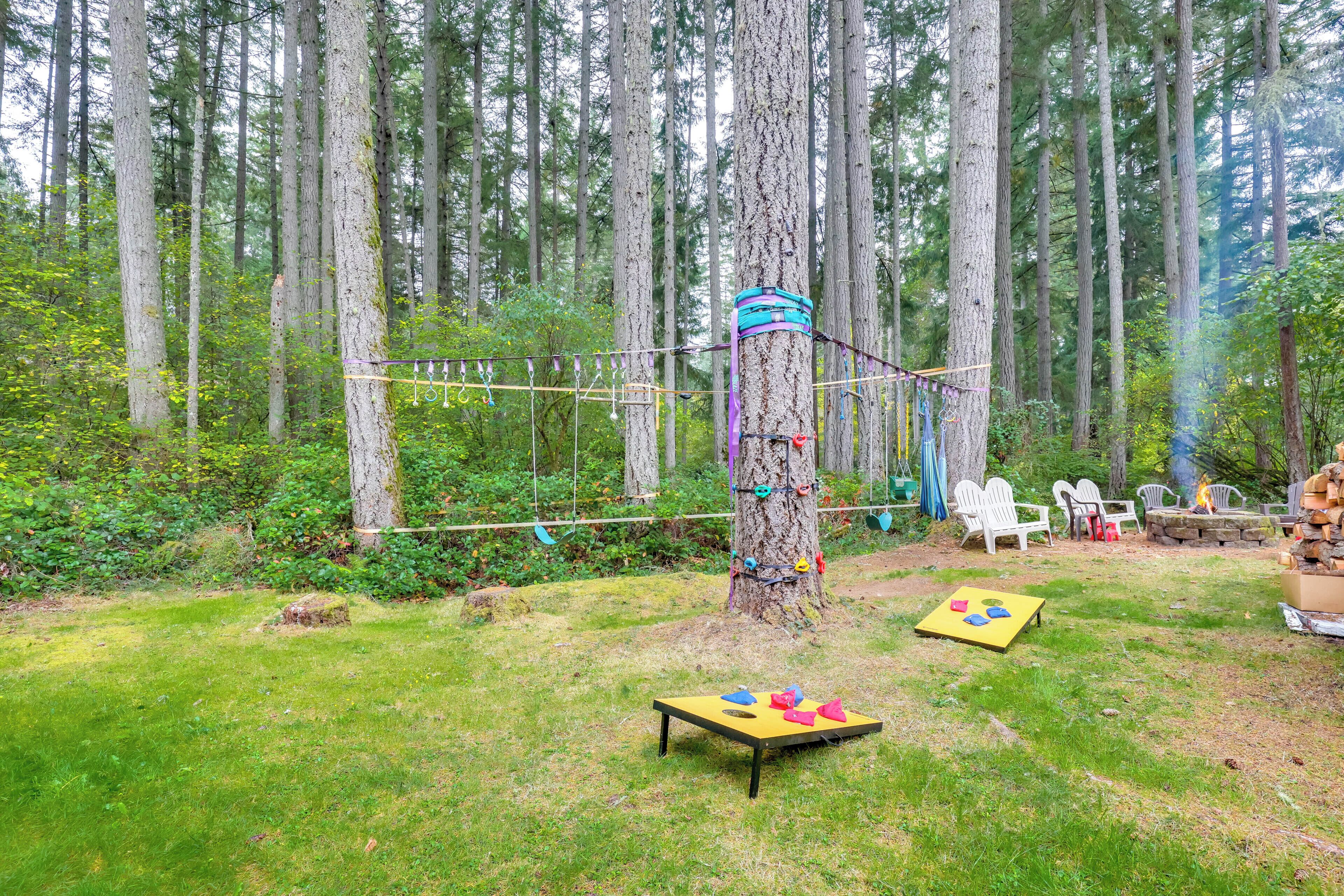 Ein bewaldetes Gebiet mit einer Lianenschaukel an einem Baum, Sitzgelegenheiten im Freien und einem Tisch mit bunten Gegenständen.