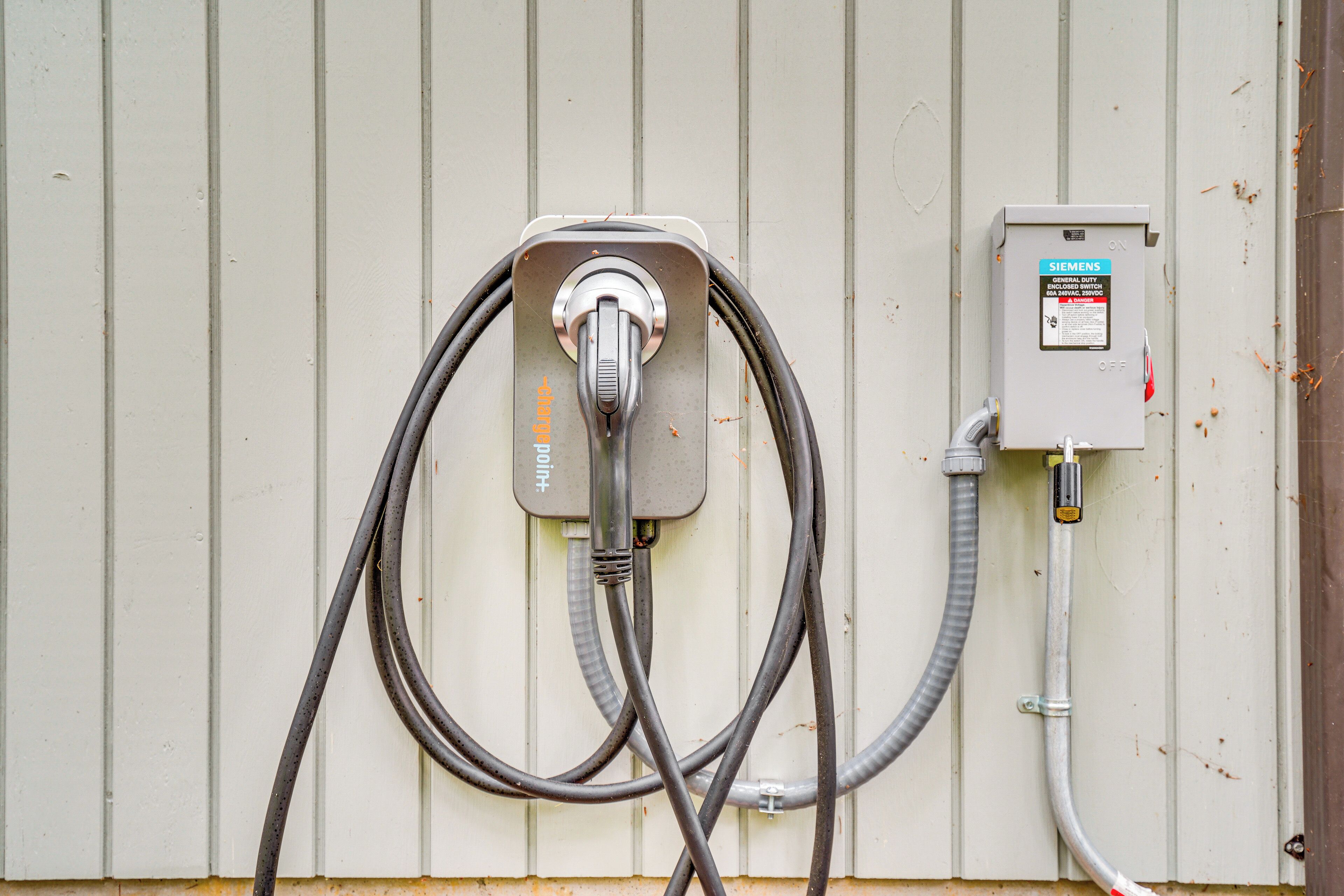 A utility meter box with multiple cables connected to it, mounted on a white wall.
