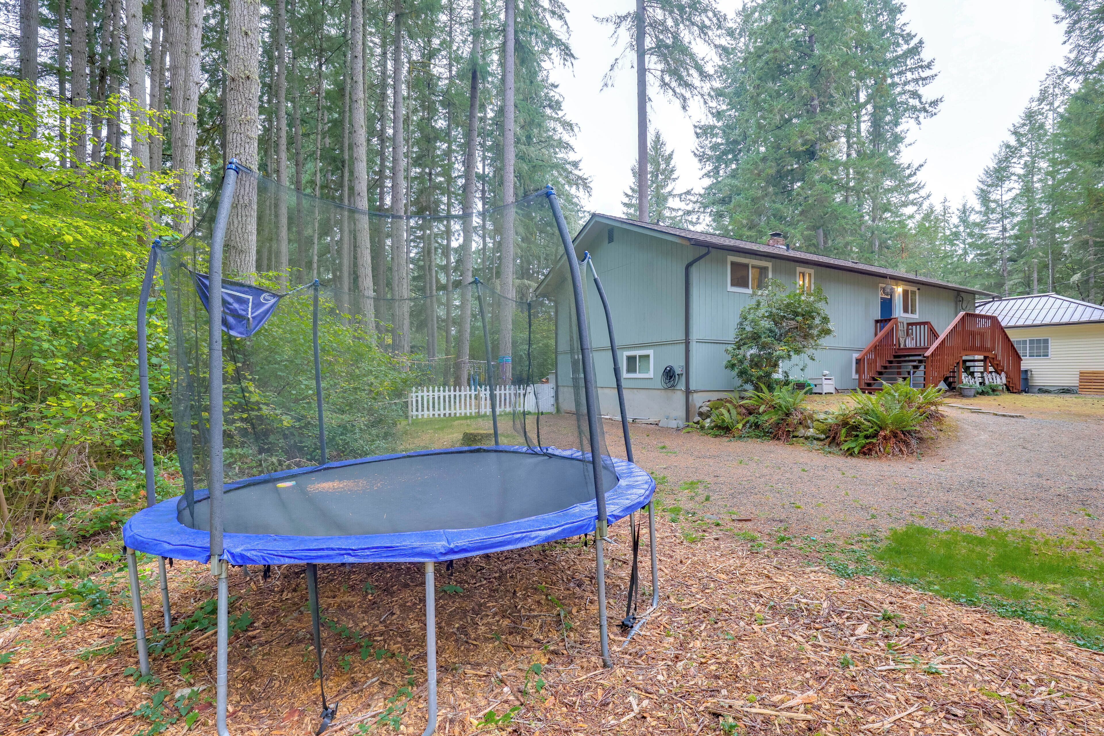A trampoline in a wooded area with a house in the background.