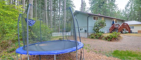 A trampoline in a wooded area with a house in the background.