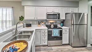 A modern kitchen with white cabinets, stainless steel appliances, and a wooden cutting board with kitchen utensils. - Coastal Myrtle Beach Condo w/ Pool ~ 5 Mi to Beach (Myrtle Beach)