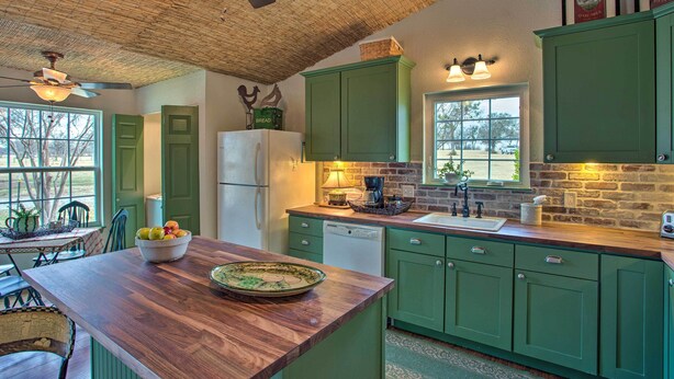 Una cocina con armarios verdes, encimera de madera, ventilador de techo y ventana con vistas.
