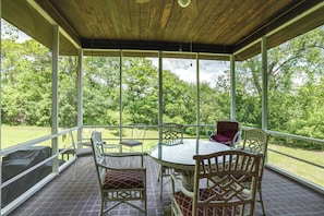 Eine überdachte Terrasse im Freien mit einem Glastisch und Stühlen, umgeben von einem Holzboden und Blick auf eine üppige grüne Landschaft.
