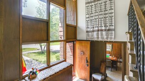 Una habitación con un ventanal grande, un banco de madera, un tapiz estampado y una escalera.