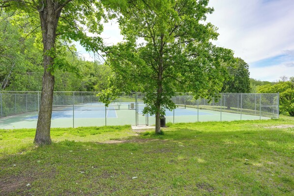 A tennis court surrounded by a chain-link fence, with trees and grass in the foreground.