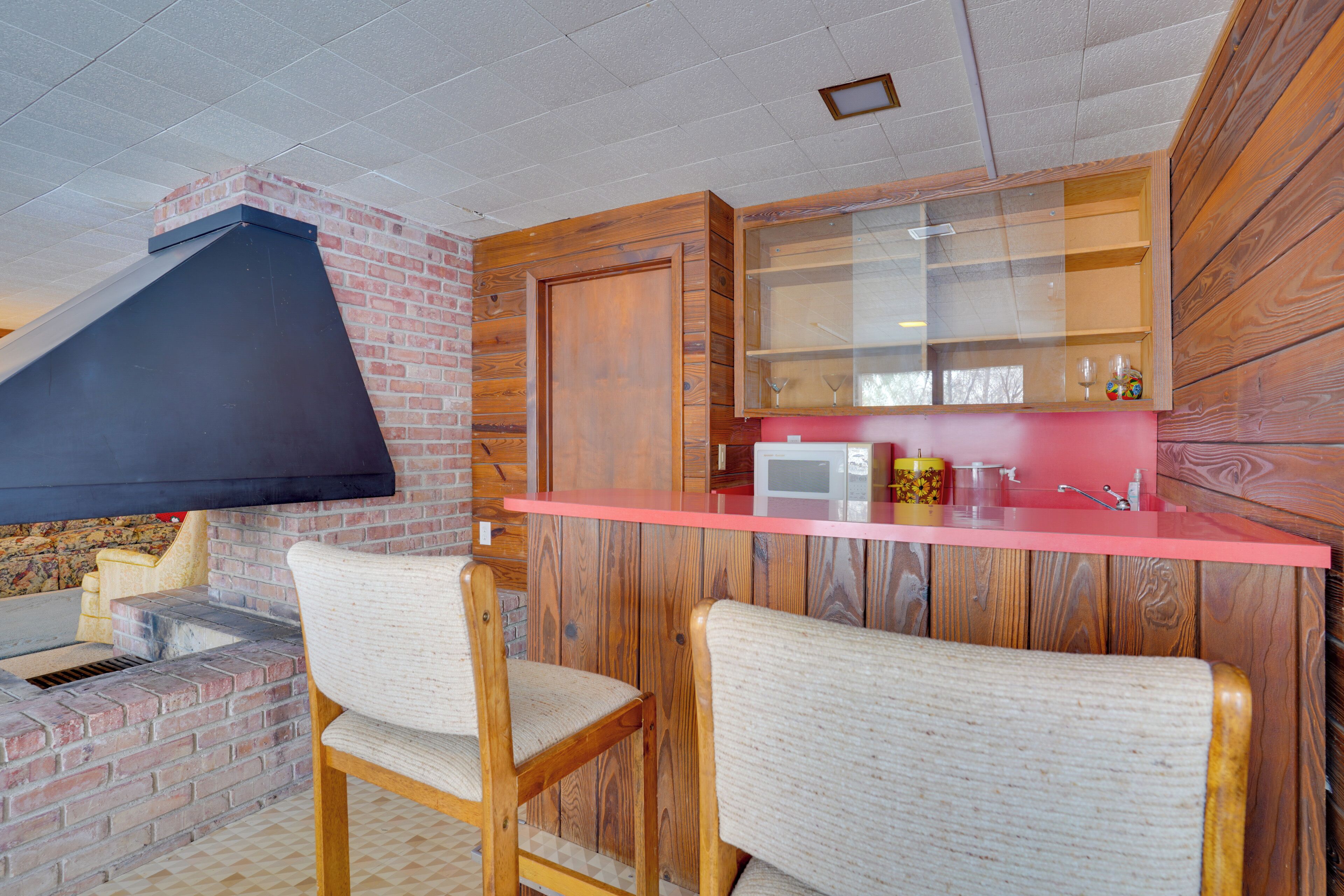 Una cocina con pared de ladrillo, armarios de madera, encimera roja y dos taburetes de bar.