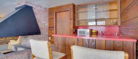 Una cocina con pared de ladrillo, armarios de madera, encimera roja y dos taburetes de bar.