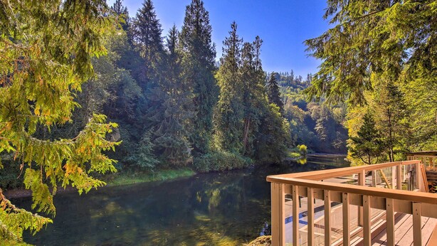 A clear view of a river surrounded by dense forest, a wooden deck, and a clear sky. - Spacious Kalama Studio w/ Riverfront Deck! (Kalama)