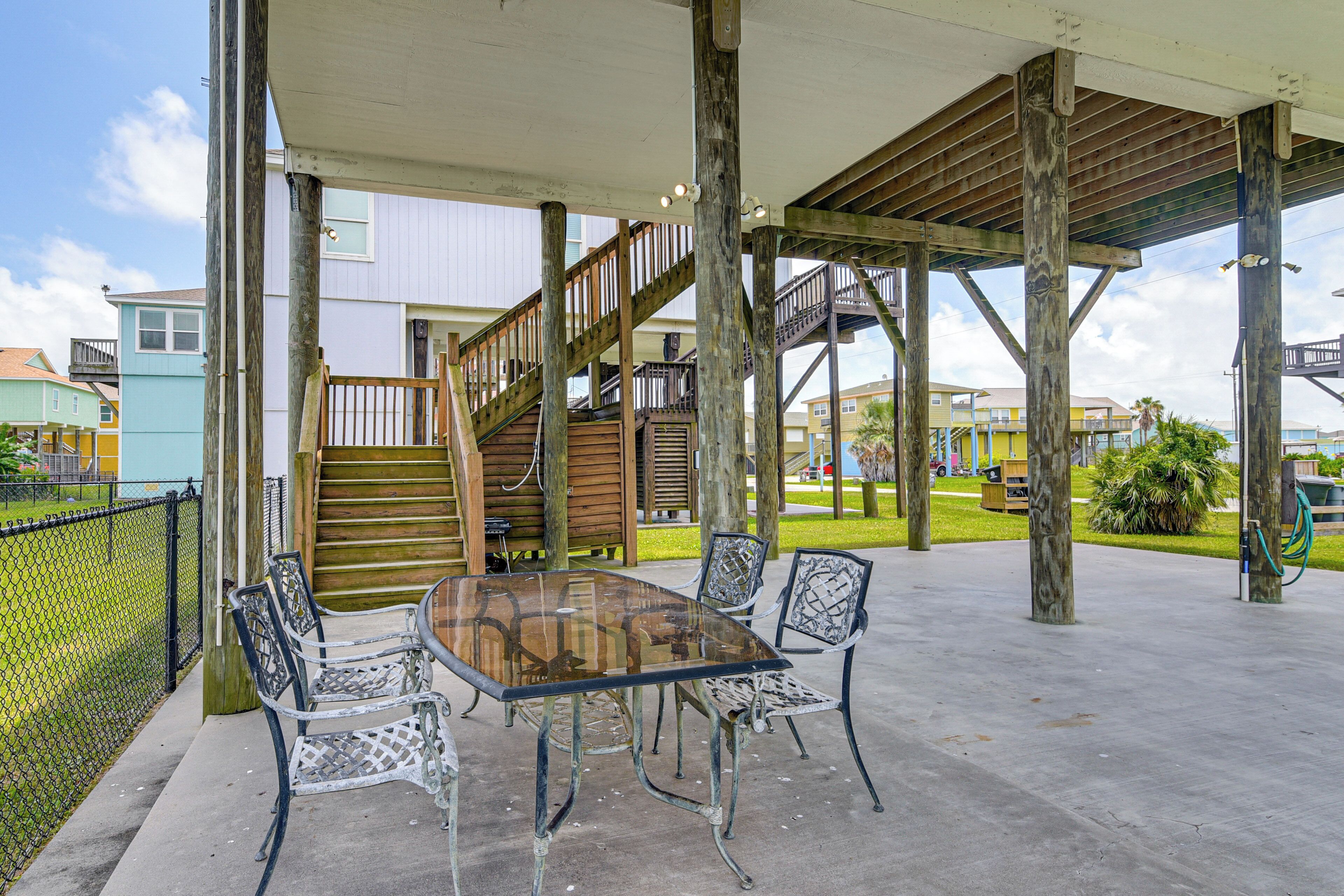 An outdoor patio with a glass table and metal chairs, wooden stairs, and a covered walkway.