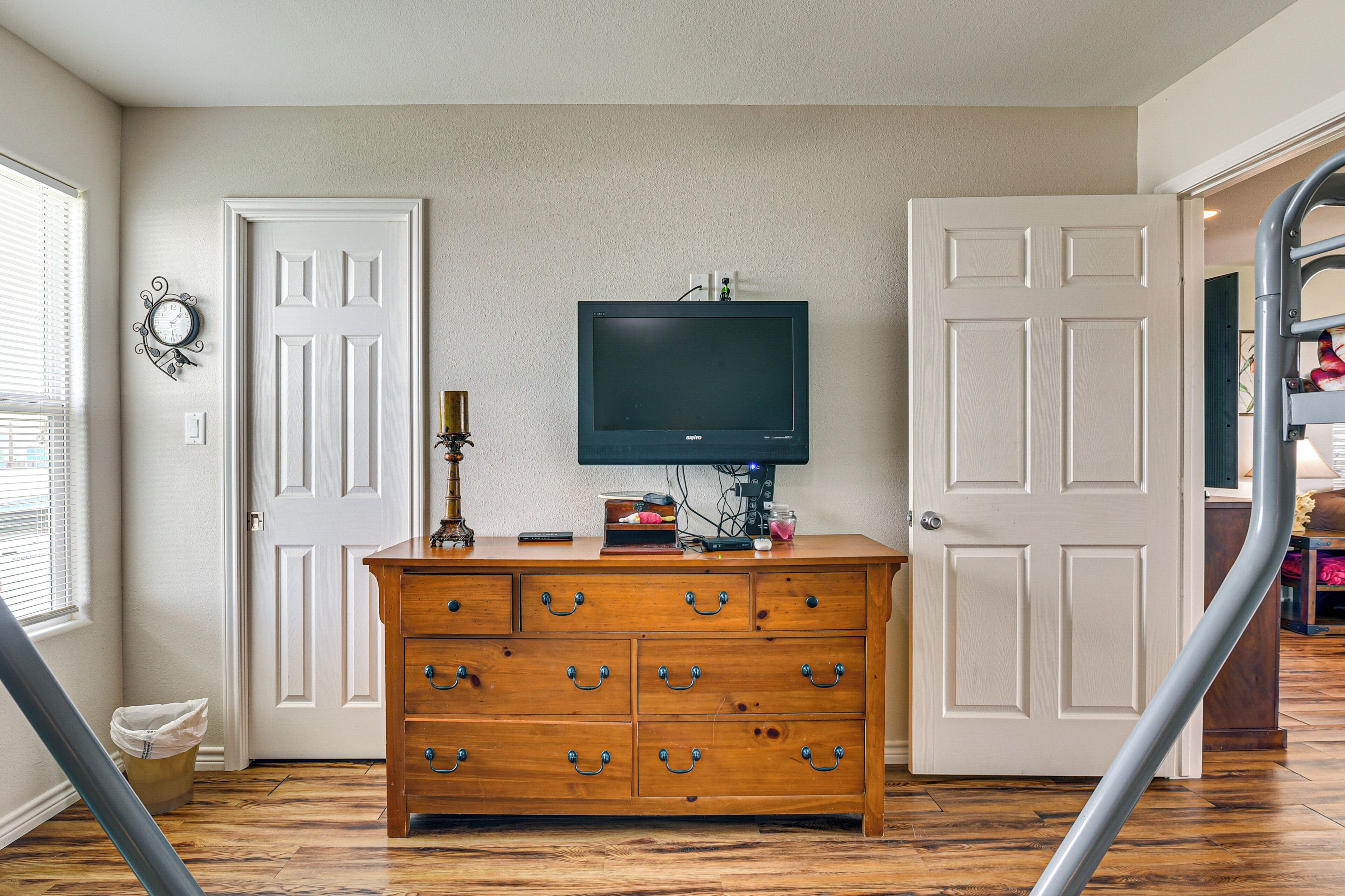 A room with a wooden dresser, a television on the wall, and two white doors.