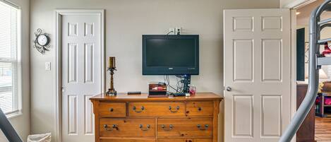A room with a wooden dresser, a television on the wall, and two white doors.
