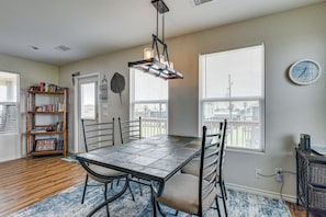 A dining area with a table, chairs, a hanging light fixture, a bookshelf, and a clock on the wall.