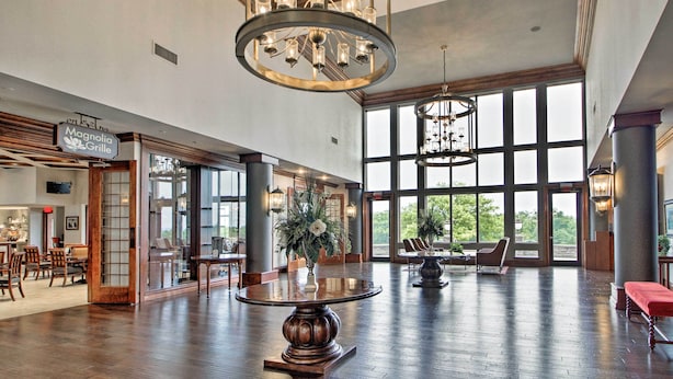 A spacious lobby with a large wooden table, a chandelier, and large windows offering a view of the outdoors. - Group Winter Retreat! Stunning Villa Near SDC (Branson)