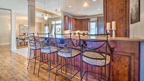A kitchen with wooden cabinets, a bar area with stools, and pendant lighting. - Group Winter Retreat! Stunning Villa Near SDC (Branson)