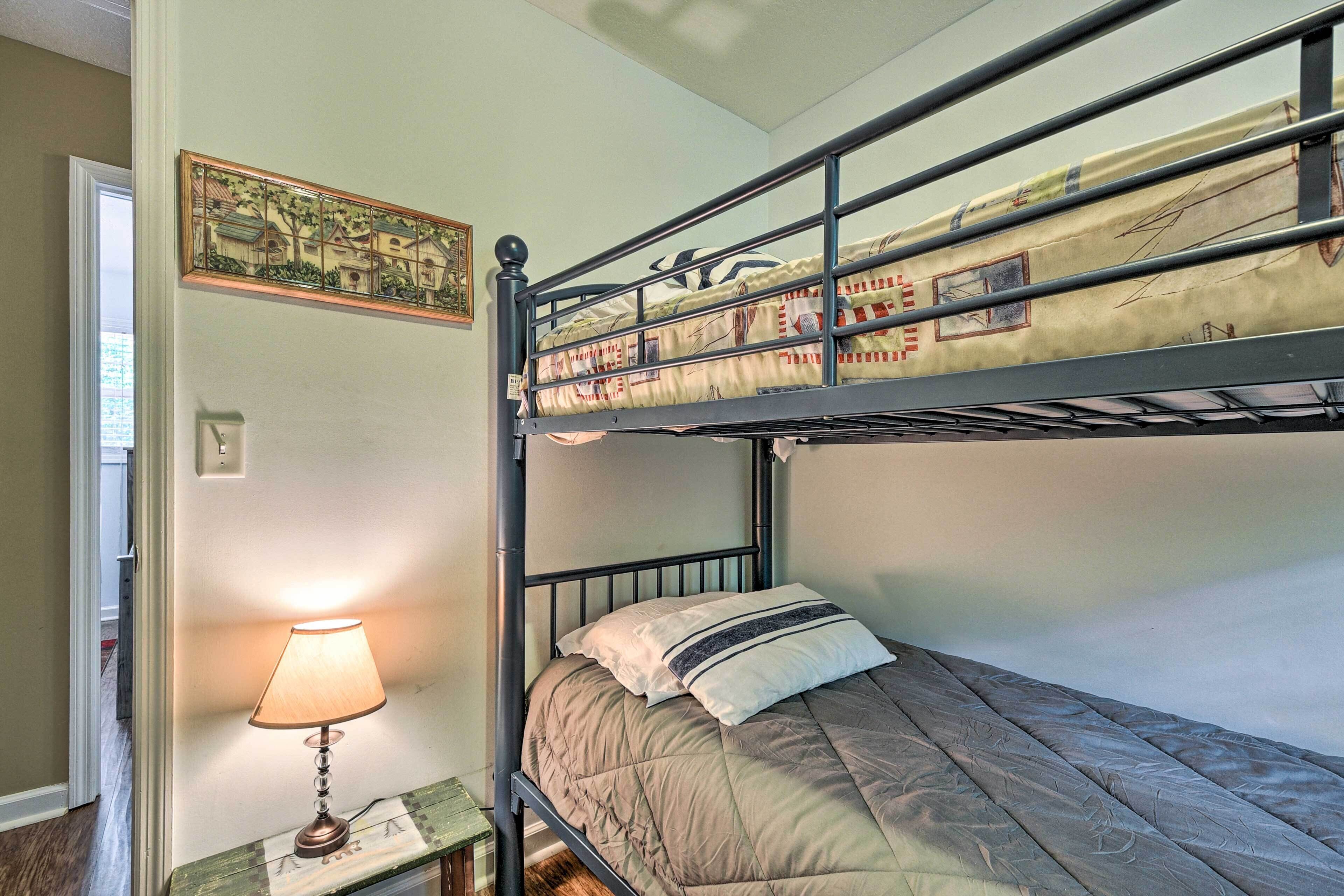 Un lit superposé avec une lampe sur une table de chevet, un tableau au mur et une porte sur le côté gauche.