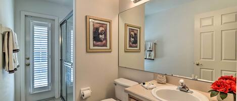 Un baño con inodoro, lavabo y espejo. Hay dos cuadros enmarcados en la pared, una puerta con ventana y una alfombra en el suelo.