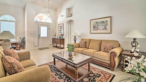 A spacious living room with a beige sofa, a wooden coffee table, and a patterned rug. There is a door leading to another room, and a framed picture on the wall. - 12 Miles to Disney: Clermont Villa w/ Heated Pool (Clermont)