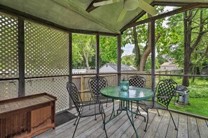 Eine überdachte Terrasse im Freien mit einer Holzbank, Metallstühlen und einem Glastisch.