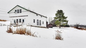 A white two-story house with a green roof, surrounded by snow-covered ground and sparse vegetation. - Historic Carriage House < 20 Mi Elk Mtn: Hike, Ski (Lakewood)