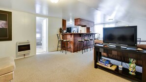 A living room with a TV, a fireplace, and a kitchen area with bar stools. - Historic Carriage House < 20 Mi Elk Mtn: Hike, Ski (Lakewood)