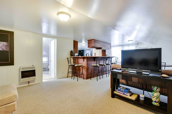 A living room with a TV, a fireplace, and a kitchen area with bar stools. - Historic Carriage House < 20 Mi Elk Mtn: Hike, Ski (Lakewood)