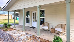 A covered porch with two wicker chairs and a small table, a white door, and a window. - Spacious Gulfport Home w/ Yard: 1 Mi to Beach (Gulfport)