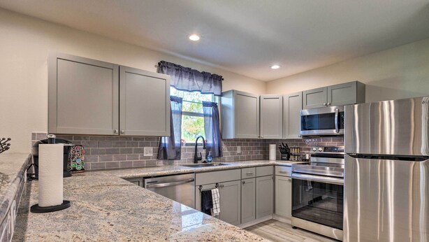 A modern kitchen with granite countertops, stainless steel appliances, and grey cabinetry. - Spacious Gulfport Home w/ Yard: 1 Mi to Beach (Gulfport)