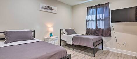 A bedroom with two beds, a ceiling fan, a TV mounted on the wall, and a window with curtains.
