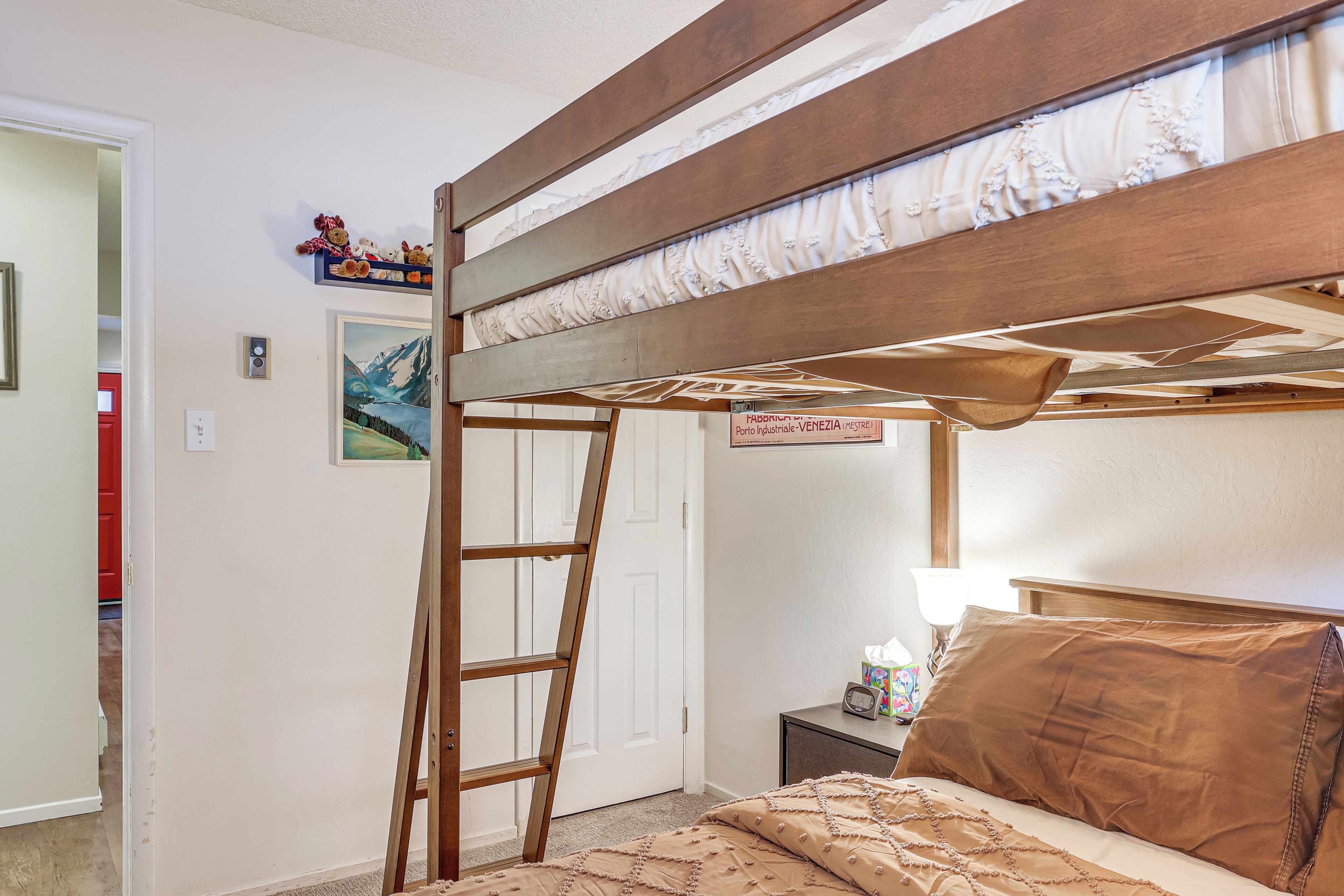 Una cama individual superpuesta con una escalera, una mesita de noche con lámpara, y un cuadro en la pared.