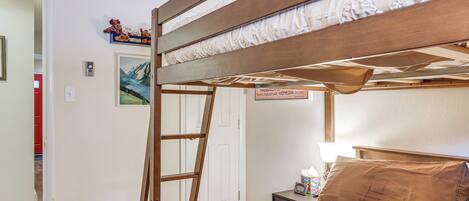 A bunk bed with a ladder, a bedside table with a lamp, and a framed picture on the wall.
