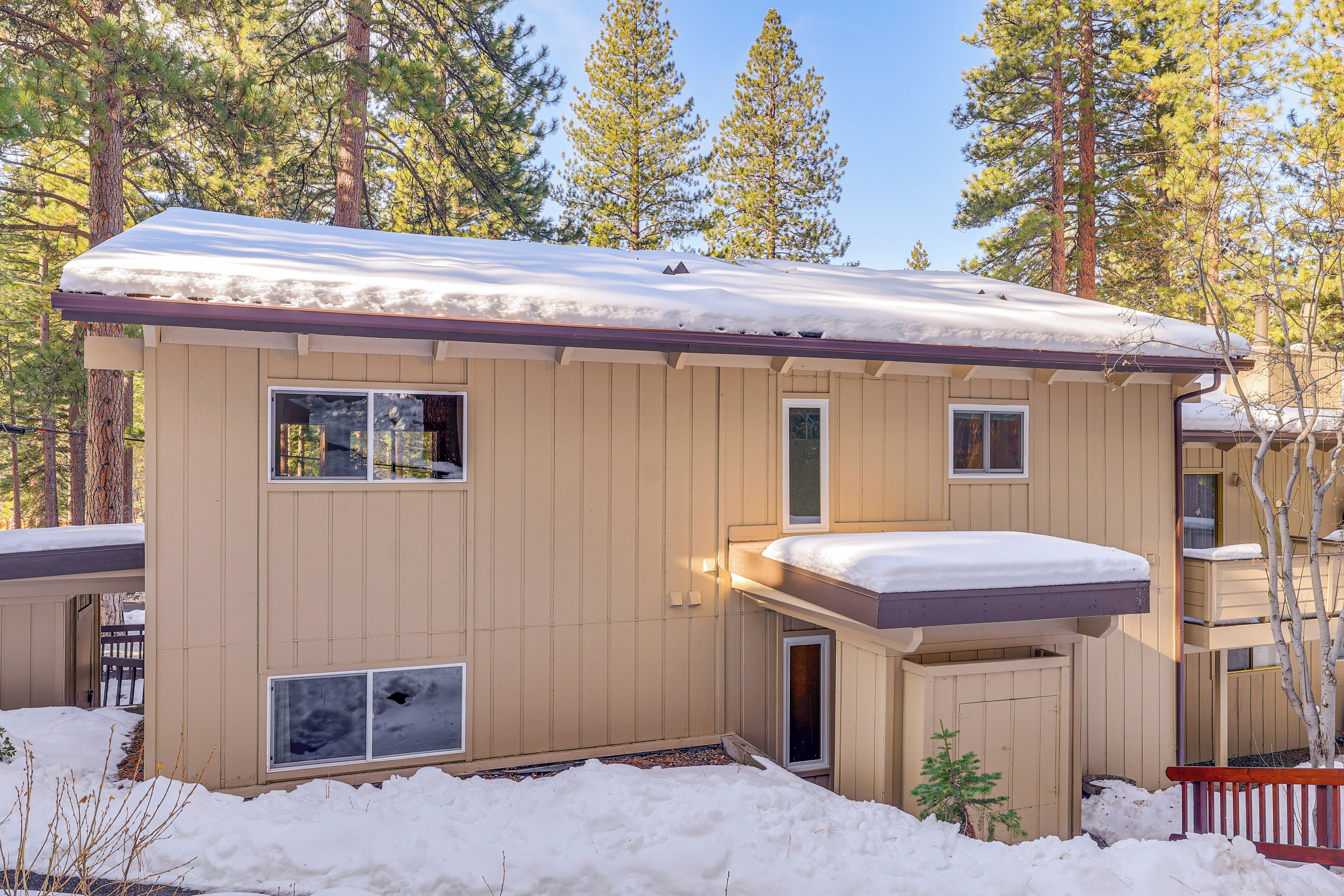 A two-story cabin with a snow-covered roof, a small porch, and a window overlooking a snowy yard.