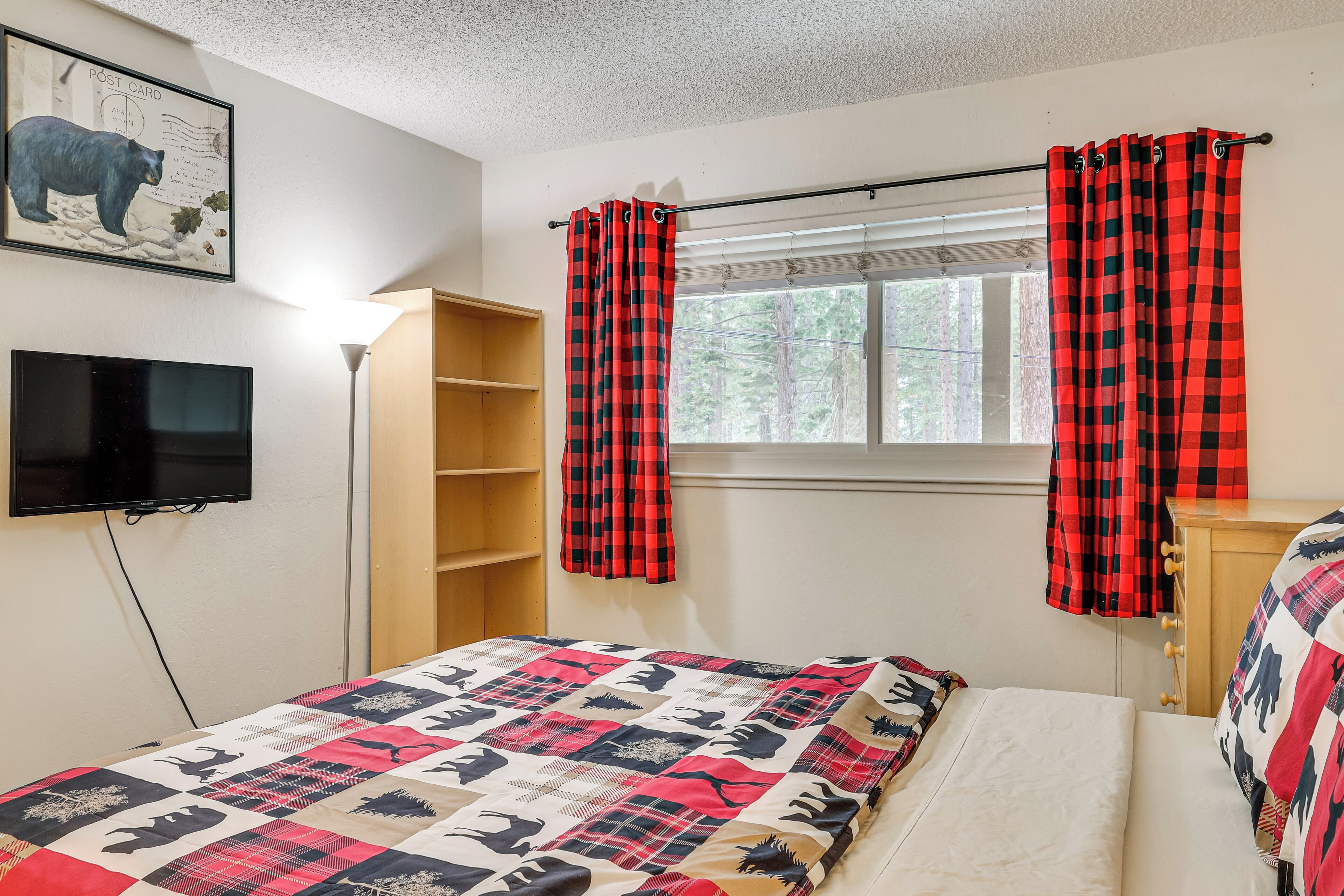 A bedroom with a bed, a television, a window with curtains, and a bookshelf.