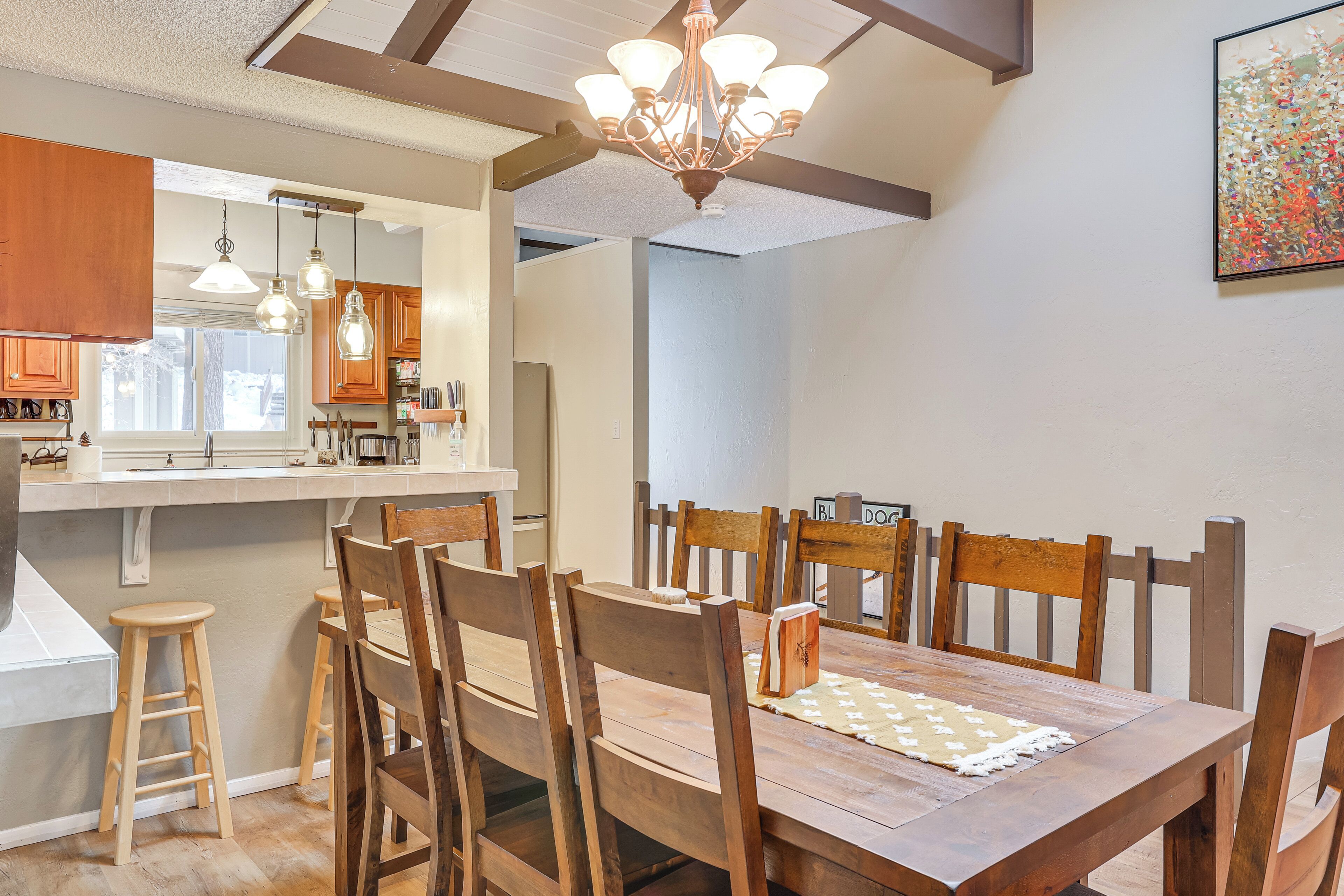 Un comedor con sillas y mesa de madera, una cocina con armarios de madera, y una araña.