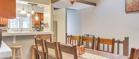 Un comedor con sillas y mesa de madera, una cocina con armarios de madera, y una araña.