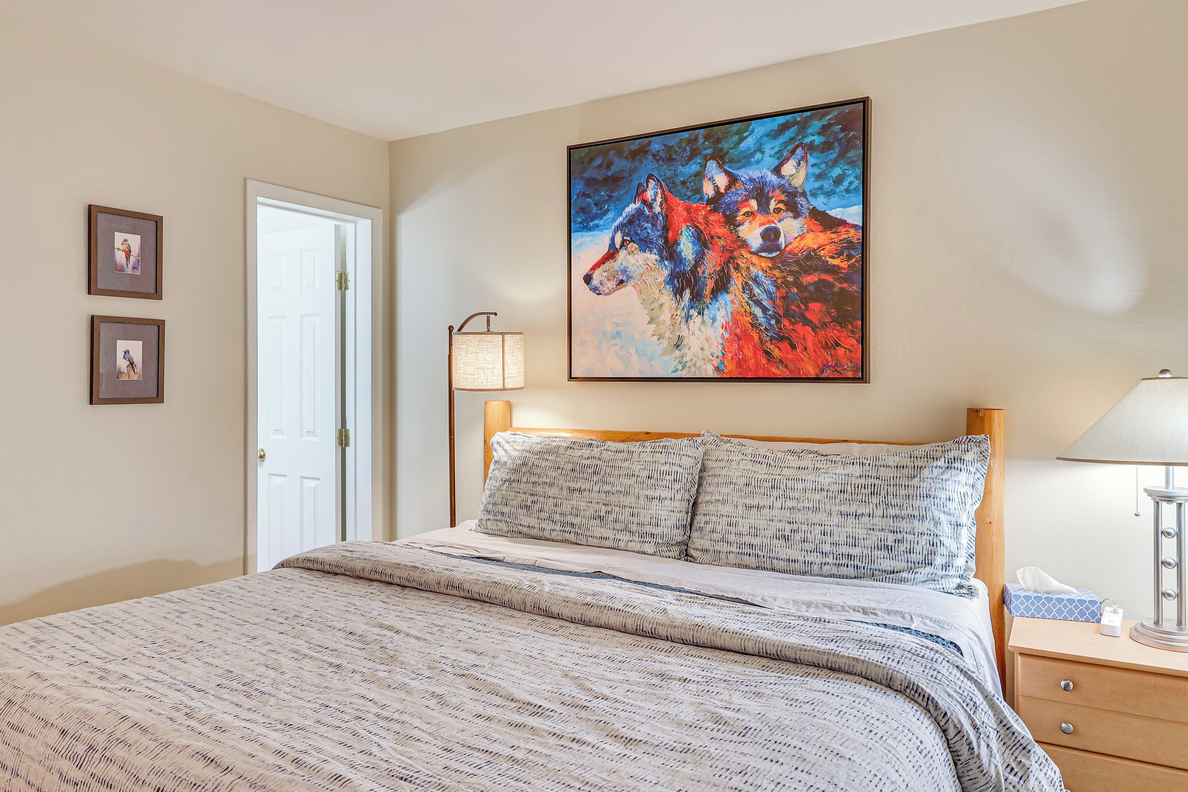 Een netjes opgemaakt bed met een beddegoed met patroon, een schilderij van wolven aan de muur en een bedlampje.