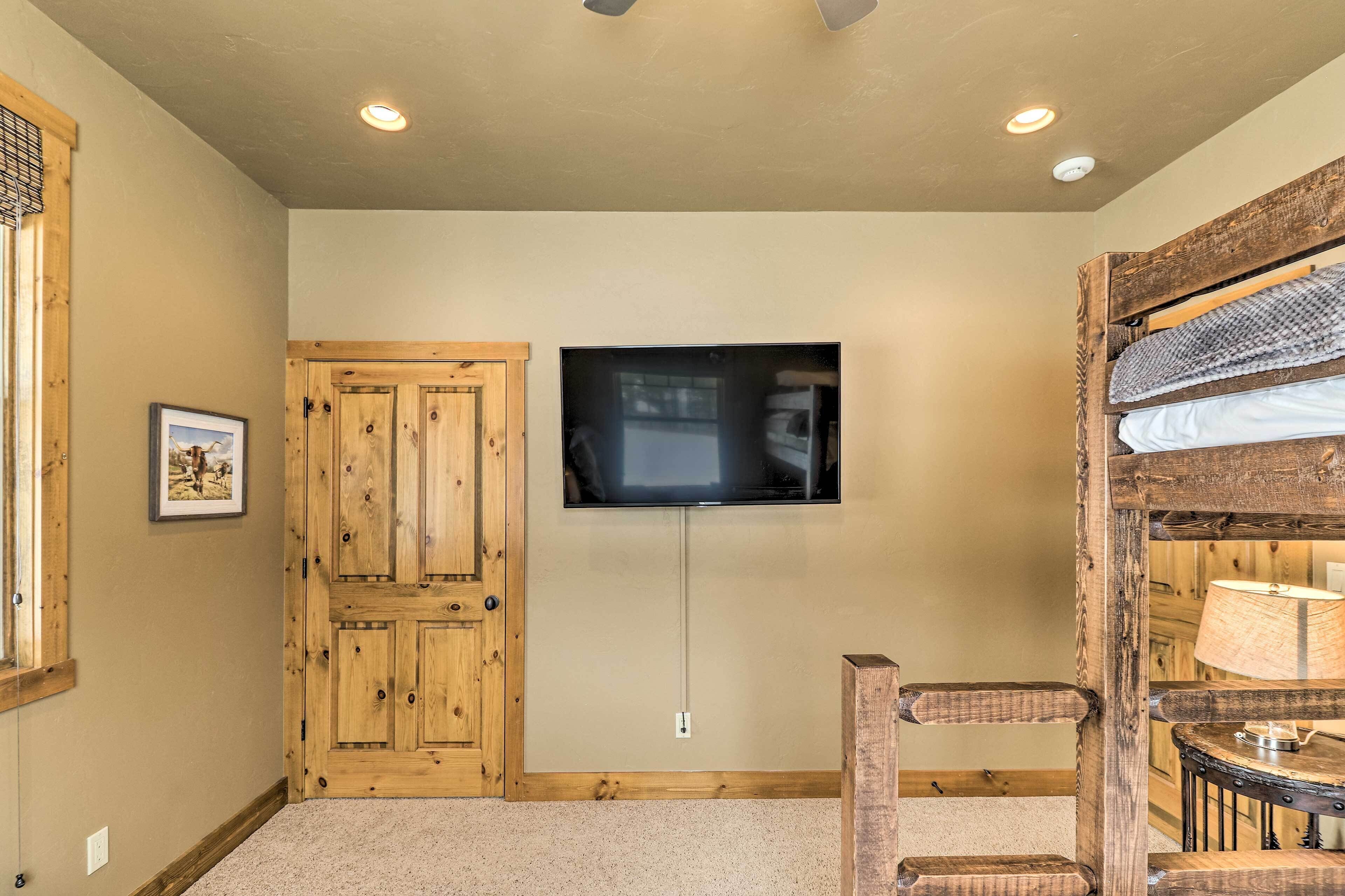 A room with a wooden door, a mounted television, and a bunk bed with a lamp.