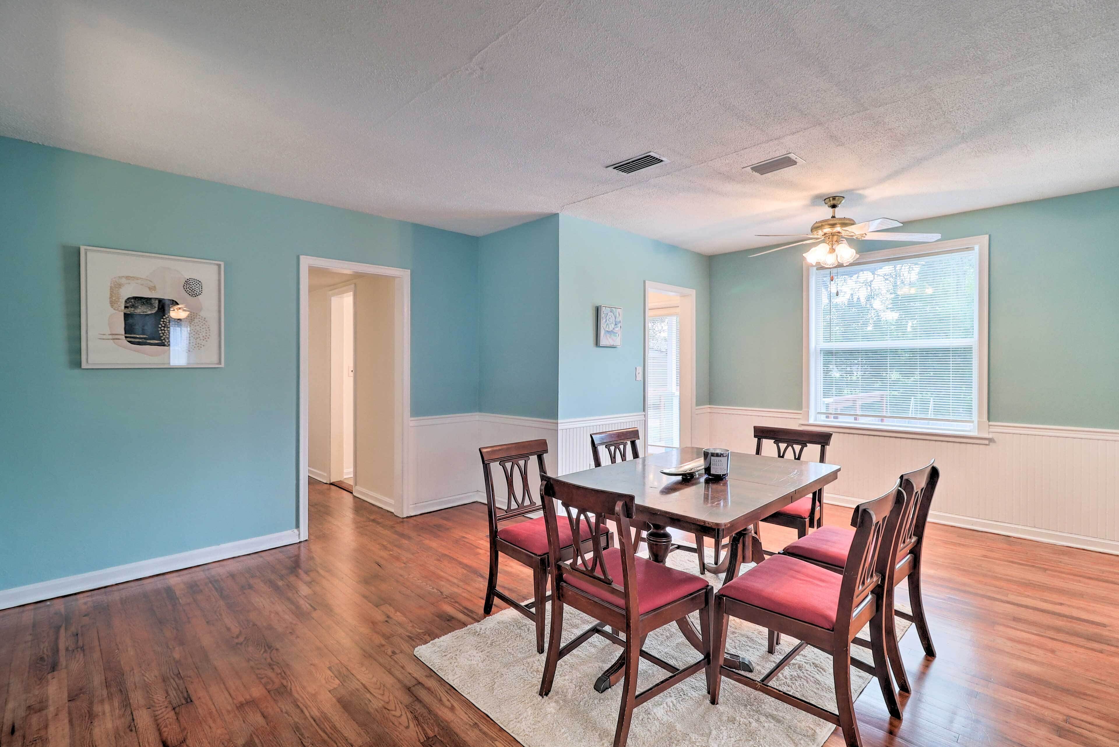 A dining area with a wooden table and chairs, light blue walls, and hardwood flooring.